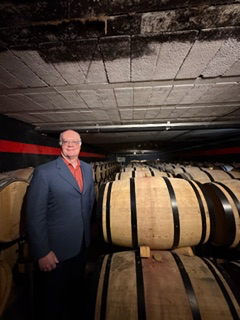 Brian beside stacked oak barrels in a stone wine cellar